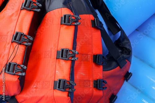 Foto Bright orange life jacket with black buckles on blue inflatable raft, close up s