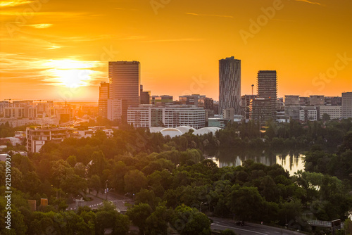 Panoramic sunset view over modern business district skyline and lush green park in Bucharest Romania during warm golden hour