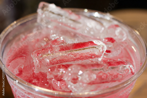 Pink fruit drink with clear ice cubes glistening in plastic cup, refreshing cold beverage with condensation and bright color
