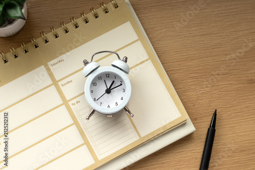 Clock and weekly planner notebook on a wooden desk. The concept of business goals, time management, and productivity.