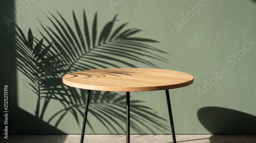 Empty round wooden table against a green wall with palm leaf shadows in a minimalist interior setting