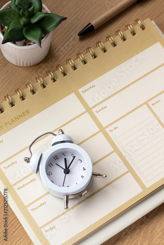 Alarm clock and weekly planner notebook on a wooden desk. The concept of goals, time management, and productivity.