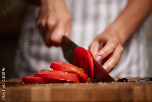 Preparing ingredients slicing fresh tomato on wooden board
