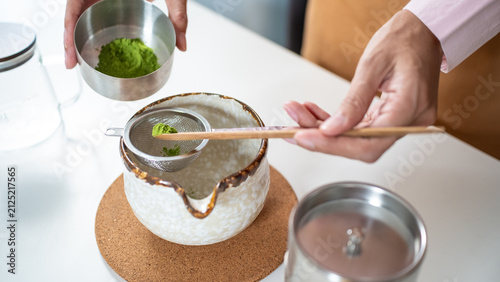 Фотография Close-up of hands using a wooden scoop to sift organic matcha green tea powder through a metal strainer into a ceramic bowl