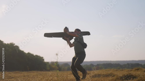 man UAV pilot with plane drone in hands preparing to launch drone in field at summer evening. warm sunset light and sun flares in frame. technology and engineering in modern warfare.