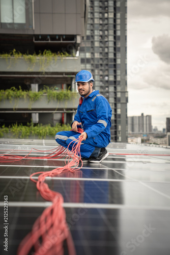 Solar Technician Routes and Organizes Electrical Cables Across Rooftop Photovoltaic Panels During Renewable Energy System Installation on an Urban Building