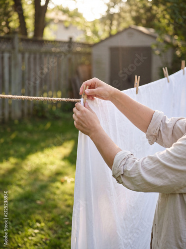 Woman hanging clean white laundry on outdoor clothesline in sunlit yard
