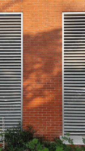 Fotografie Red brick wall background with symmetrical metal louver vents and sunlight shado
