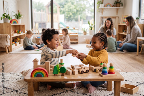 Two preschool children engage in free play, sharing wooden toys at a preschool. Other children and adults are visible in the background during this fun learning time