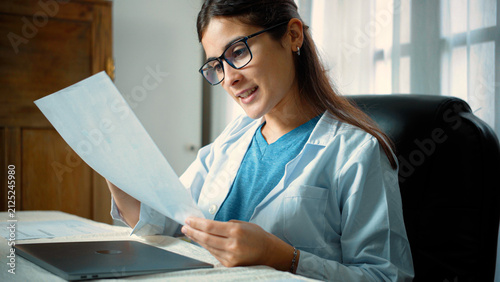 Young Latina female nurse looking happy while reviewing medical test results, representing positive patient outcomes, clinical analysis, professional satisfaction, and compassionate healthcare.