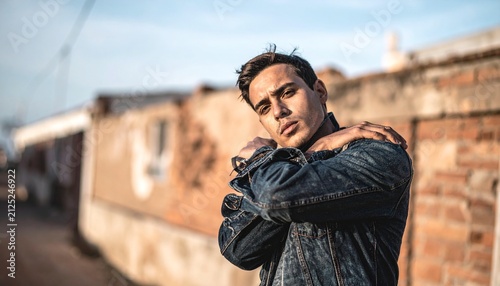 Man in denim jacket posing outdoors with brick wall background