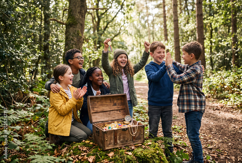 A group of children smiles and cheers in a forest after finding a treasure chest. They are enjoying their time together in nature