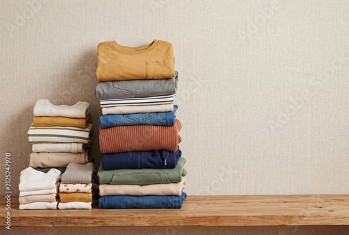 A stack of children's clothes is neatly folded and organized by size from baby to school age. The background is warm and neutral, providing a simple display for the clothes