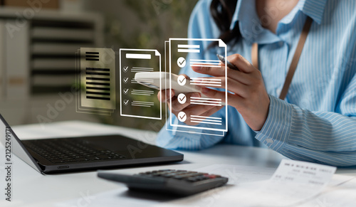 Business woman using smartphone for online digital document management and checklist approval. Paperless office, electronic signature, financial audit concept with laptop and calculator.