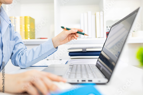 Woman analyzes charts on a laptop. She studies data with focused intent. Desk holds plants, notes, and a phone. Professional workspace with soft lighting
