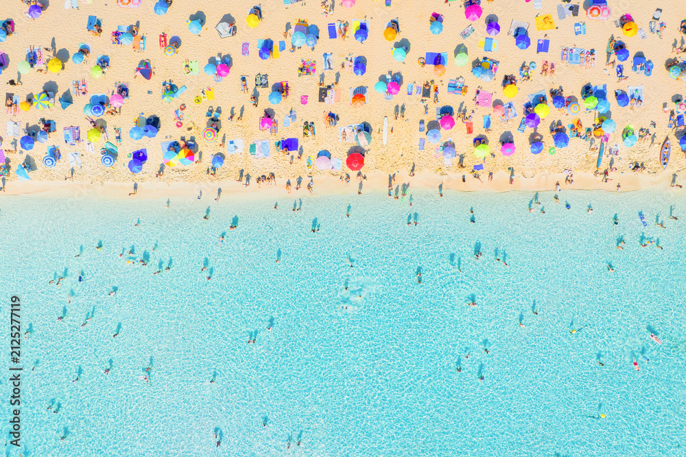 Obraz premium Aerial drone view of people relaxing on a white sand beach under colorful umbrellas. Bright sunny summer vacation scene by turquoise crystal clear sea water.