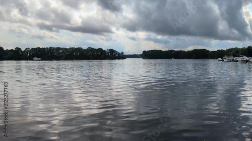 wide view of a calm lake under a dramatic, cloudy sky with gentle water ripples and treelines in the background.
