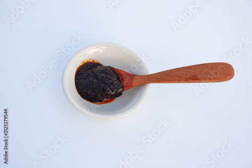 Wooden spoon scooping Thai chili paste (Nam Prik Pao) in a white bowl, top view on white background