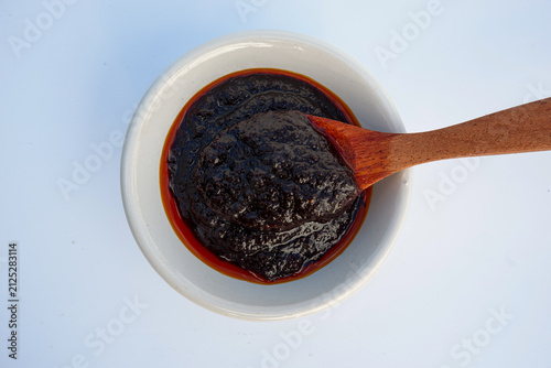 Thai chili paste (Nam Prik Pao) in a white bowl with a wooden spoon, top view on white background