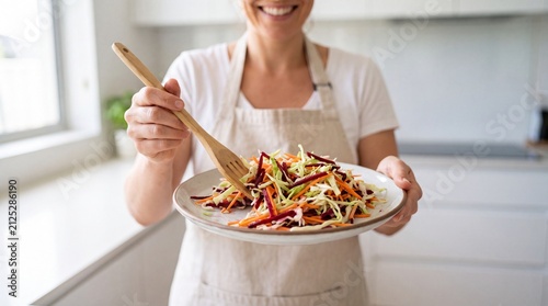 Woman presenting fresh shredded vegetable salad on plate in kitchen