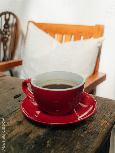 Close-up of a vibrant red coffee cup with black coffee on a rustic wooden table.