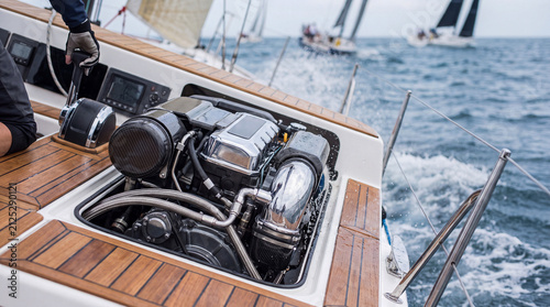 Open marine engine compartment on sailboat deck with gloved crew operating controls