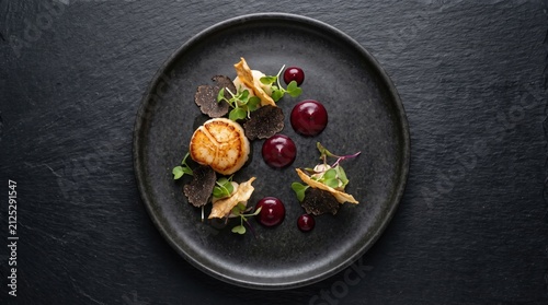 Seared scallop with truffle, microgreens and berry puree on black plate