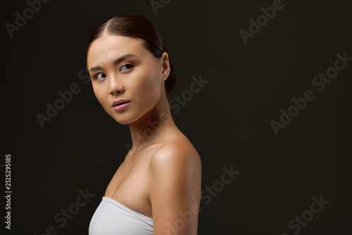 Fotografie Sensual Asian woman showcasing beauty against a grey backdrop