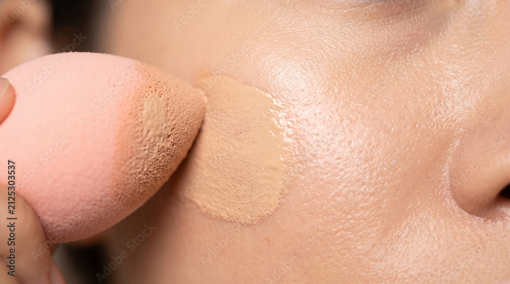 Fototapeta premium Close-up of a person using a pink makeup sponge to apply liquid foundation to their cheek, ad social media download thambnail poster web template event festival 2026 2027 2028