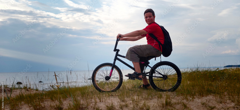 Fototapeta premium Boy rides bike on sunny path while another rider performs tricks on BMX