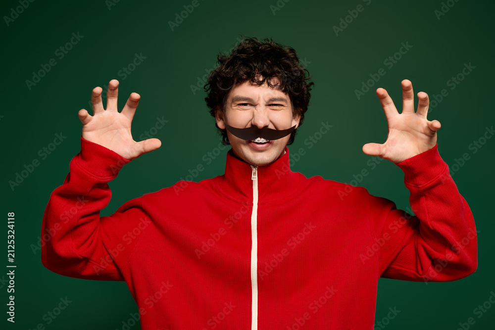 Naklejka premium Young man with a playful spirit showing off his moustache in a vibrant green backdrop