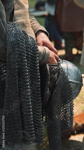 Men in medieval clothing handle pieces of chainmail and helmets in a reenactment setting. The atmosphere reflects daily life and preparation for battles typical of the early Middle Ages