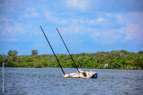 front view, far distance of, a two masted sailboat, sinking in a tropical river, with a blue sky, in late morning sunlight