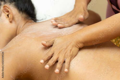 Woman receiving relaxing exfoliating body scrub treatment on back in spa