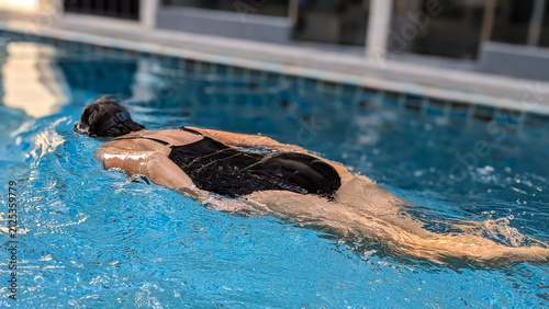 Konstfotografi Middle-aged woman swimming freestyle in a pool, viewed from behind while wearing a black swimsuit and goggles