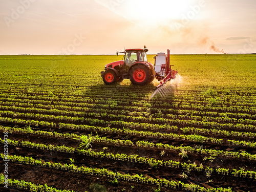Tractor spraying soybean field with pesticides at sunset