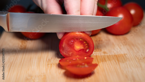 Fotografía A hand is holding a red tomato on a cutting board and slicing it with a kitchen knife