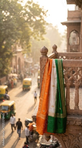 Sari fabric representing the Indian flag draped over carved stone balcony, celebrating Independence Day on August 15, showing a blurred city street background in India.