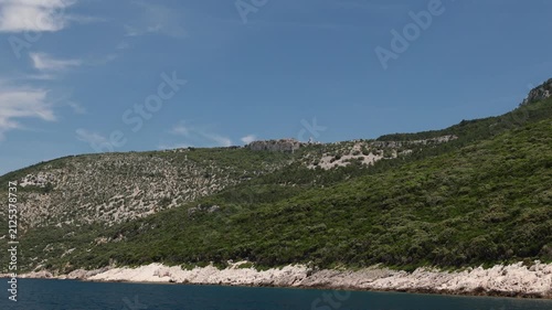 view of Lubenice historic village perched on cliffs from Sveti Ivan Beach. Providing a panoramic view of the rugged coastline. Lush green slopes. And the clear blue Adriatic Sea on Cres Island