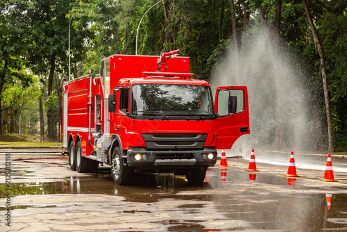 Caminhão de bombeiros vermelho em treinamento com jato de água em estrada arborizada