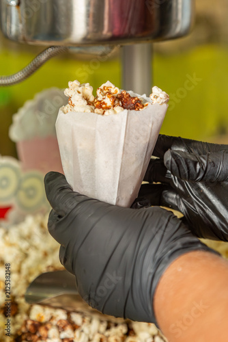Mãos com luvas pretas segurando saco de papel com pipoca caramelizada fresca