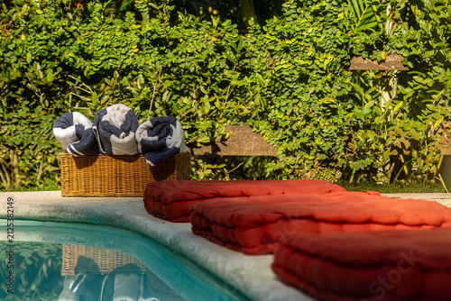 almofadas vermelhas e toalhas em cesto ao lado da piscina em jardim tropical