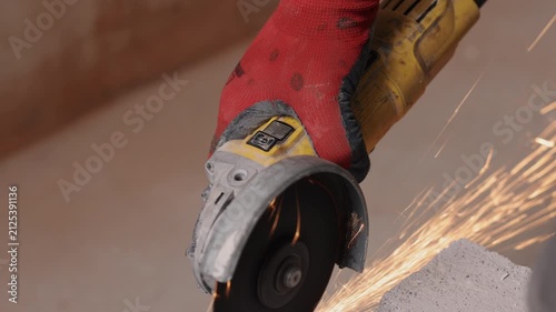 angle grinder, steel fabrication, shop floor. Close detail captures grinder cutting steel rod while shower bright sparks lights up work area.