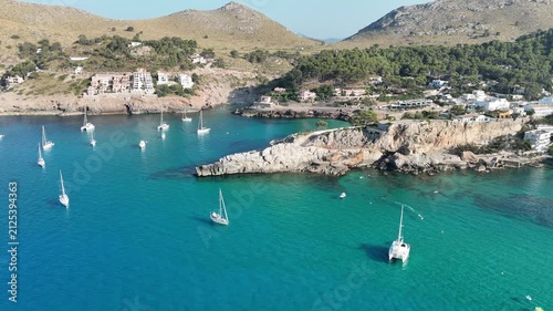 Aerial static shot panning right revealing scenic bay, turquoise waters, and anchored boats in Cala Sant Vicenc, Mallorca