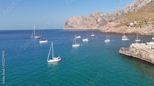 Aerial forward push-in shot over blue waters approaching anchored sailboats in Cala Sant Vicenc, Mallorca