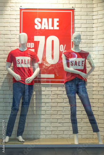 Clothing store window display with mannequins wearing red sale t-shirts and big discount sign up to 70 percent