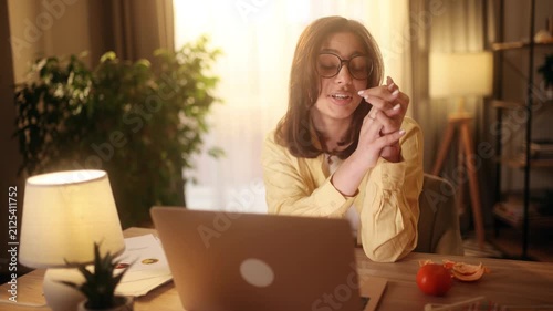 Beautiful attractive young woman in eyeglasses having a friendly video call on laptop at home. Pretty female student or freelancer smiling during online meeting in sunny room