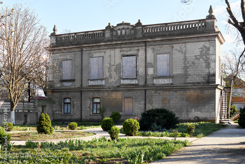 Abandoned historic building with boarded windows and overgrown garden in daylight