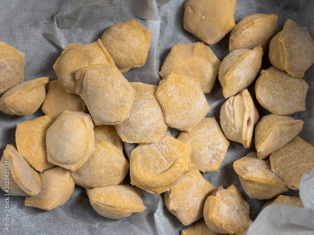 Obraz premium Freshly made, uncooked dumplings on parchment paper. Golden brown, irregularly shaped dumplings scattered across surface. Ready for cooking or baking, homemade style. Textured dough visible