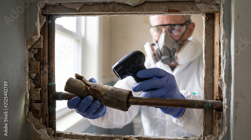 Protected inspector assesses aging pipe lagging in apartment wall